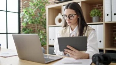Young beautiful hispanic woman business worker using touchpad and laptop at office