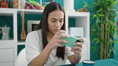 Genç, güzel İspanyol kadın yemek odasında akıllı telefonla video oyunu oynuyor.