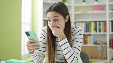 Genç ve güzel İspanyol kız öğrenci kütüphane üniversitesinde akıllı telefon kullanıyor.
