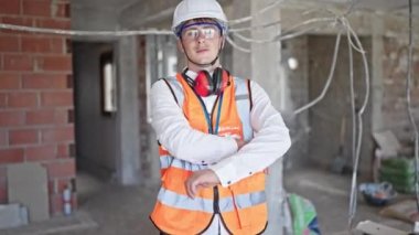 Kafkasyalı genç bir mimar gülümsüyor. Şantiyede kollarını kavuşturmuş duruyor.