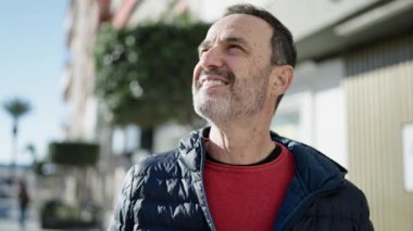 Orta yaşlı bir adam sokakta kendine güvenerek gülümsüyor.