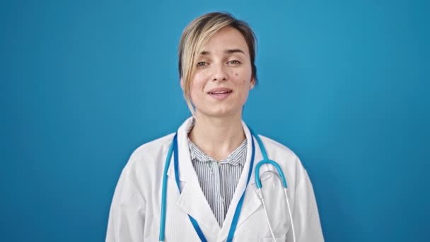 Νεαρή Ξανθιά Γυναίκα Γιατρός Χαμογελά Σίγουρος Λέγοντας Γεια Χέρι Πάνω — Αρχείο Βίντεο