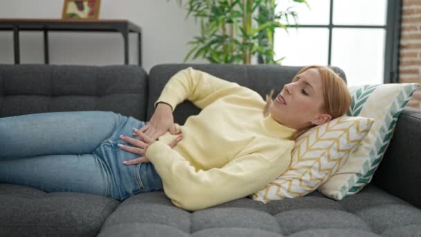 Young Blonde Woman Suffering Menstrual Pain Lying Sofa Home — 图库视频影像