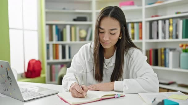 若い美しいヒスパニック女性学生使用ノートパソコン書きノートで大学教室 — ストック動画