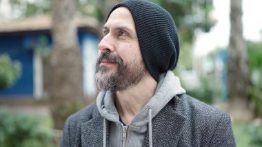 Genç kel adam parkın kenarına bakarak gülümsüyor.