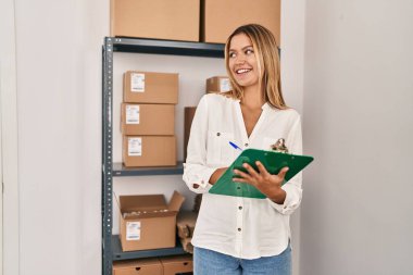 Young hispanic woman ecommerce business worker writing on document at office