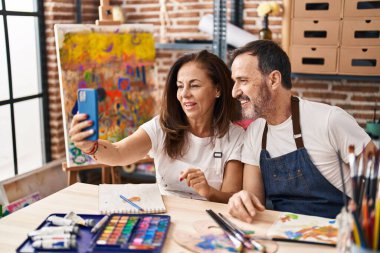 Middle age man and woman artists drawing on notebook make selfie by the smartphone at art studio