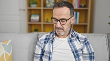 Middle age man sitting on sofa with relaxed expression at home