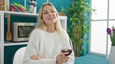 Genç sarışın kadın bir bardak şarap içip yemek odasında konuşuyor.