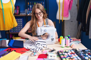 Genç bayan terzi elbise fabrikasında dikiş makinesi kullandığından emin gülümsüyor.