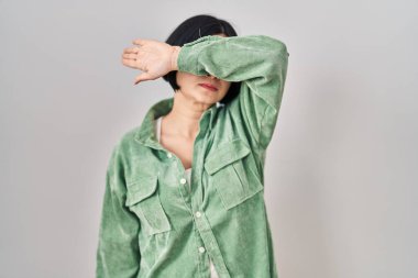 Beyaz arka planda duran genç Asyalı kadın kollarıyla gözlerini kapatıyor, ciddi ve üzgün görünüyor. Görme, saklama ve reddetme konsepti 