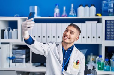 Genç İspanyol bilim adamı laboratuvarda akıllı telefonun yanında selfie çekiyor.