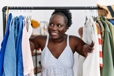 Young african american woman customer appearing throw clothes rack at clothing store