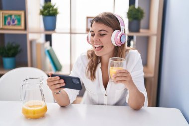 Young woman watching video on smartphone drinking orange juice at home