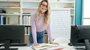 Genç sarışın kadın öğretmen sınıfta kendine güvenen bir şekilde not defterine yazıyor.