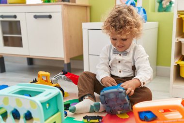 Sevimli sarışın çocuk arabalarla oynuyor. Anaokulunda yerde oturuyor.