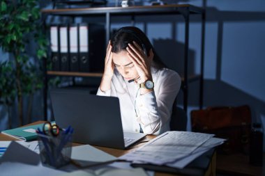 Çağrı merkezi kulaklığı takan genç esmer kadın gece geç saatlere kadar çalışıyor. Ağrı ve migren yüzünden baş ağrısı çekiyor ve stresli. Eller başının üstünde.. 