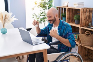 Evde tekerlekli sandalyede oturan İspanyol bir gencin elinde yeni evin anahtarı var.