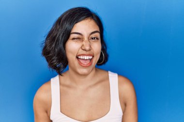 Mavi arka planda duran genç İspanyol kadın kameraya seksi bir ifadeyle bakıyor, neşeli ve mutlu bir yüzle.. 