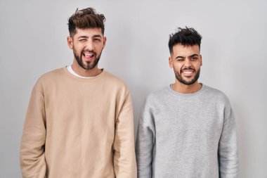 Genç homoseksüel çift beyaz arka planda durup kameraya seksi bir ifadeyle, neşeli ve mutlu bir yüzle bakıyor.. 
