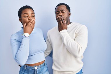 Mavi arka planda dikilen genç Afro-Amerikan çift ağızlarını elleriyle kapatmaktan sıkıldı. Huzursuz ve uykulu.. 