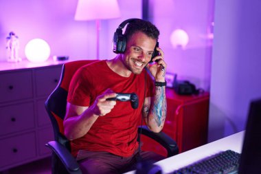 Young hispanic man streamer playing video game using joystick at gaming room