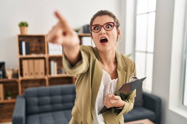 Muayenehanede çalışan genç bir kadın parmağıyla işaret ederek şaşırmış, ağzı açık, şaşırmış, ön tarafta bir şey var. 