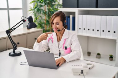 Orta yaşlı doktor kadın kulaklık takıyor. Gülümsüyor, el ve parmağıyla işaret ediyor. 