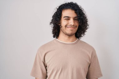 Beyaz arka planda kıvırcık saçlı İspanyol bir adam kameraya seksi bir ifadeyle bakıyor, neşeli ve mutlu bir yüzle.. 