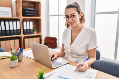 Genç, güzel İspanyol iş kadını. Ofisteki evraklarda dizüstü bilgisayar kullanıyor.