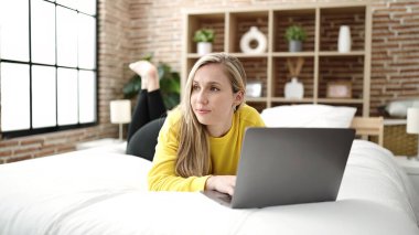 Yatak odasında dizüstü bilgisayar kullanan genç sarışın kadın.