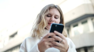 Sokakta akıllı telefon kullanan, kendine güvenen genç sarışın kadın.