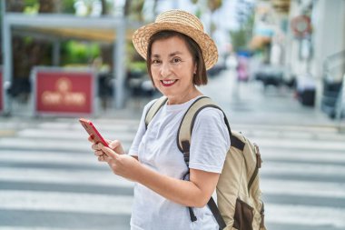 Orta yaşlı bir turist sokakta akıllı telefon kullanarak gülümsüyor.