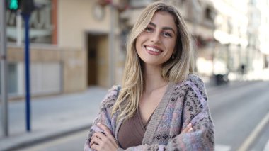 Sokakta kollarını kavuşturmuş genç sarışın kadın.