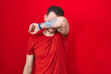 Genç İspanyol bir adam kırmızı arka planda dikiliyor. Gözleri kollarıyla kapatıyor, ciddi ve üzgün görünüyor. Görme, saklama ve reddetme konsepti 