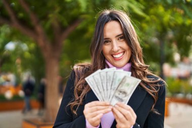 Young hispanic woman smiling confident holding dollars at park