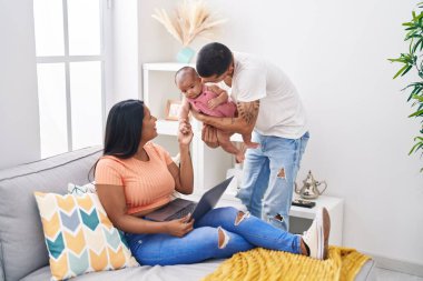 Evdeki kanepede oturan İspanyol aile dizüstü bilgisayar kullanıyor.