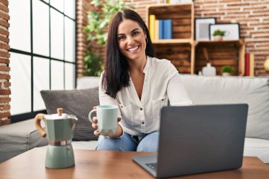 Genç ve güzel İspanyol kadın dizüstü bilgisayar kullanıyor. Evde kahve içiyor.