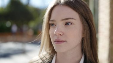 Sokakta ciddi bir ifadeyle yan tarafa bakan genç sarışın kadın.