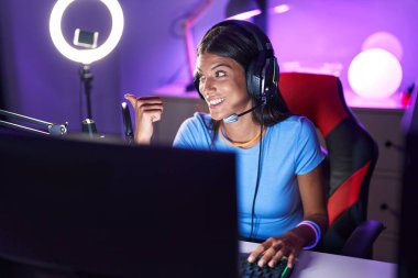 Kumral, video oyunları oynayan, gülen, gülümseyen ve baş parmağıyla yan tarafı gösteren genç bir kadın.. 