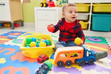 Anaokulunda yerde taşaklarıyla oynayan sevimli sarışın çocuk.