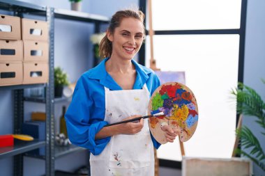 Young woman artist holding paintbrush and palette at art studio