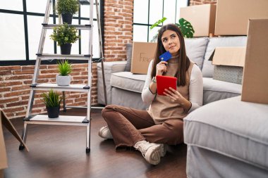 Genç, İspanyol bir kadın dokunmatik ped ve kredi kartı kullanıyor. Yeni evinde yerde oturuyor.