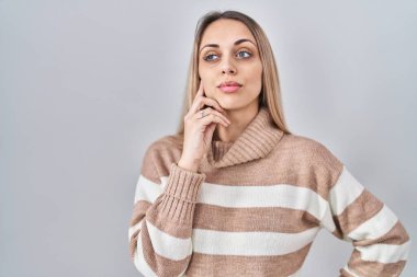 Young blonde woman wearing turtleneck sweater over isolated background with hand on chin thinking about question, pensive expression. smiling with thoughtful face. doubt concept.  clipart