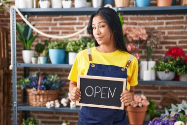 Çiçekçide çalışan İspanyol kadın açık tabela tutuyor. Gülümsüyor ve başka tarafa bakıyor.. 