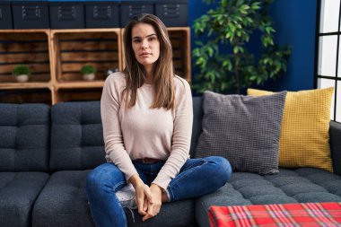 Yüzünde ciddi bir ifadeyle evdeki kanepede oturan güzel bir kadın. Basit ve doğal bir şekilde kameraya bakıyorsun.. 