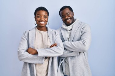 Genç Afro-Amerikan çift mavi arka planda yan yana durmuş kollarını kavuşturup kameraya bakarken gülümsüyor. pozitif kişi. 