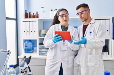 Man and woman wearing scientist uniform using touchpad at laboratory