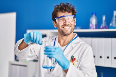 Young man scientist smiling confident pouring liquid on test tube at laboratory