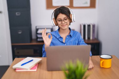 Ofisteki gözlüklü genç kız parmaklarıyla imza atıyor, gülümseyerek mükemmel bir sembol oluşturuyor. 